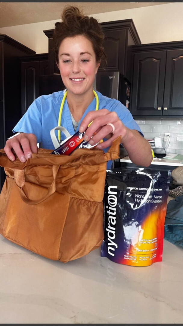 Person in a kitchen holding a brown bag with a Nydration drink mix package on a counter.
